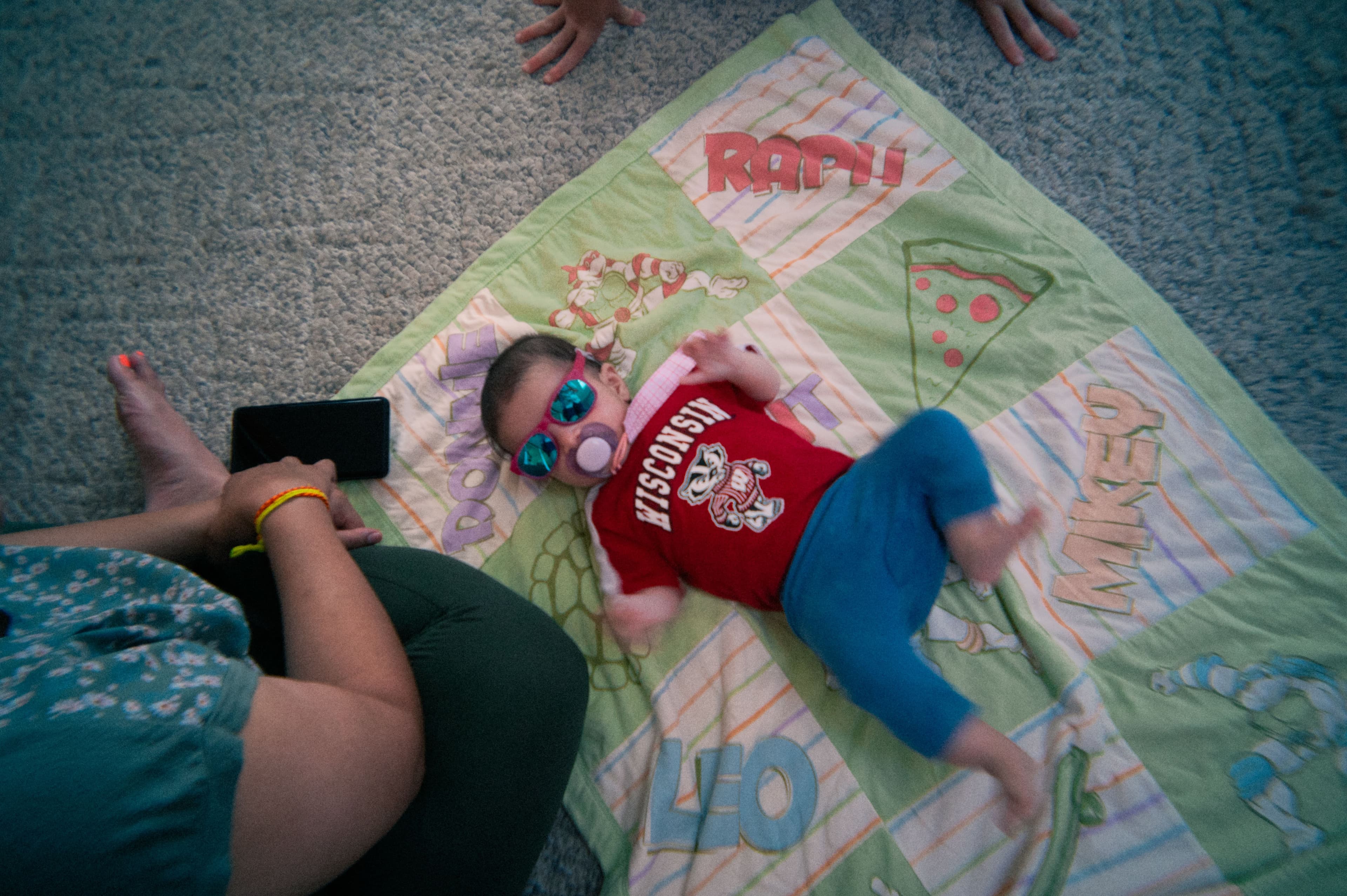 a baby in sunglasses laying on a TMNT blanket